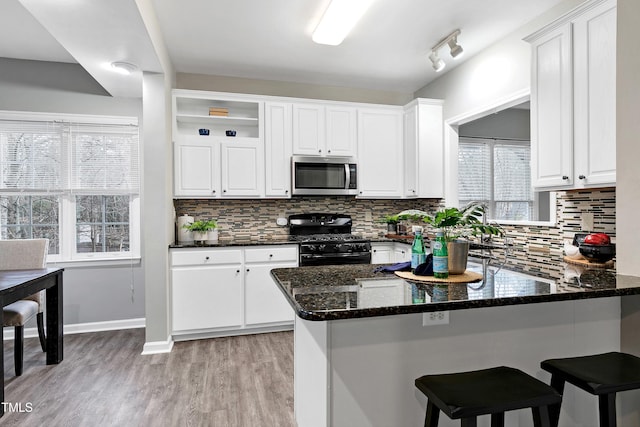 kitchen featuring stainless steel microwave, gas stove, white cabinets, dark stone counters, and a peninsula