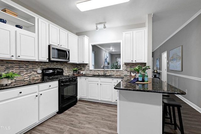 kitchen with crown molding, stainless steel microwave, black gas stove, wood finished floors, and a kitchen bar