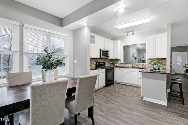 kitchen with black gas range, light wood finished floors, white cabinets, dark countertops, and stainless steel microwave