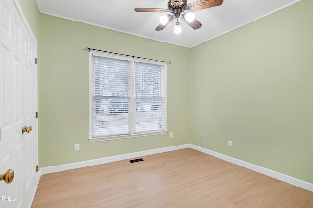 empty room with visible vents, crown molding, light wood-style flooring, and baseboards