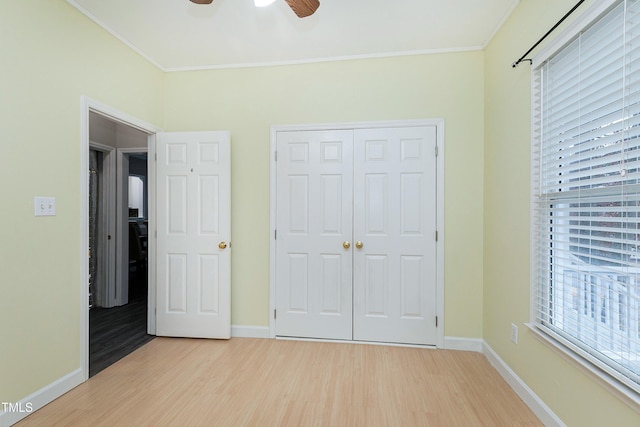 unfurnished bedroom featuring ceiling fan, wood finished floors, baseboards, a closet, and crown molding