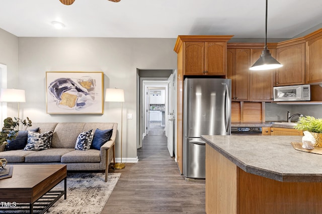 kitchen featuring brown cabinetry, wood finished floors, freestanding refrigerator, hanging light fixtures, and a sink