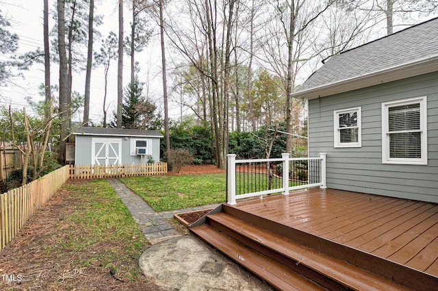 wooden deck with a storage unit, fence, a lawn, and an outbuilding