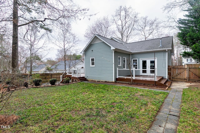 rear view of property with a shingled roof, fence, a deck, and a yard