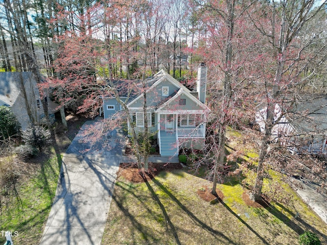 view of front of property featuring a chimney, a porch, concrete driveway, stairway, and a front lawn