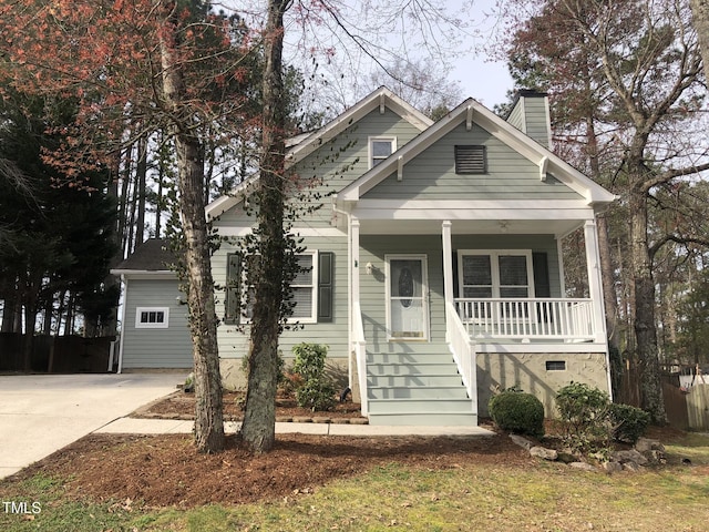 view of front of home featuring covered porch, concrete driveway, and a chimney