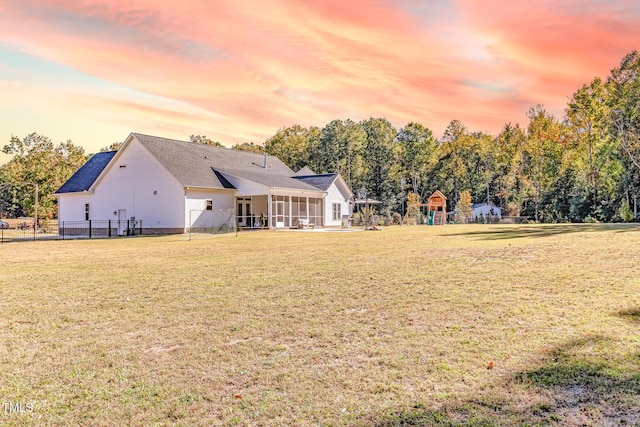 back of property featuring a sunroom, a playground, a lawn, and fence