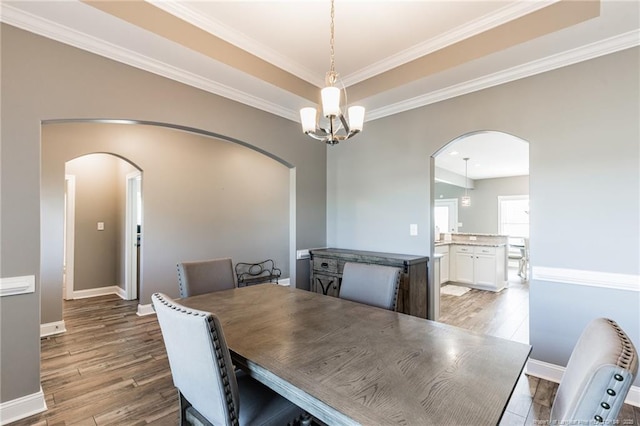 dining area with arched walkways, a tray ceiling, baseboards, and light wood-style floors