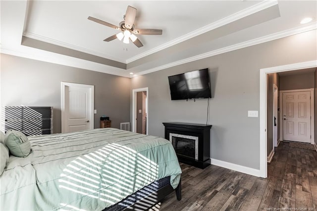 bedroom with crown molding, a tray ceiling, dark wood finished floors, and baseboards