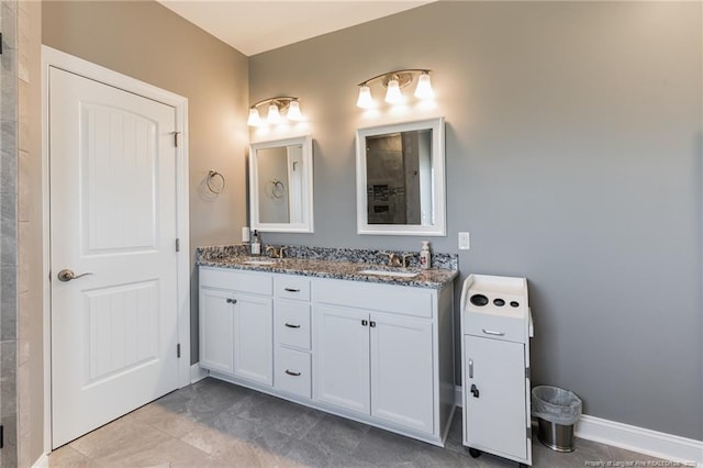 bathroom featuring tiled shower, a sink, baseboards, and double vanity