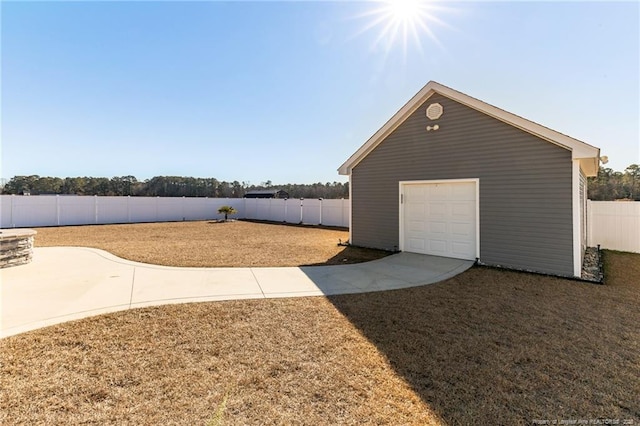 view of yard featuring driveway, a fenced backyard, a detached garage, and an outdoor structure