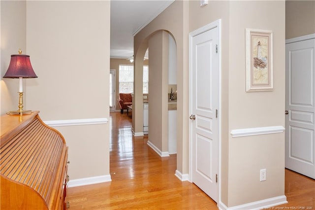 hallway featuring arched walkways, light wood-style flooring, and baseboards