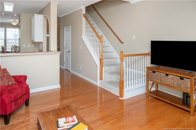 living room with light wood-style floors, ornamental molding, stairway, and baseboards