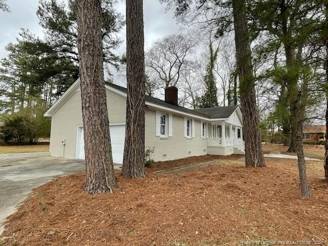 view of side of property featuring a garage, concrete driveway, crawl space, stucco siding, and a chimney