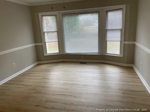 empty room with light wood-type flooring, crown molding, and baseboards