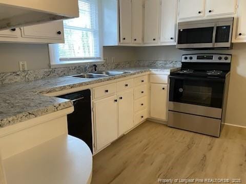 kitchen with appliances with stainless steel finishes, a sink, white cabinets, and light wood-style floors