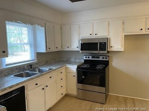 kitchen featuring white cabinets, light wood-style flooring, appliances with stainless steel finishes, light countertops, and a sink