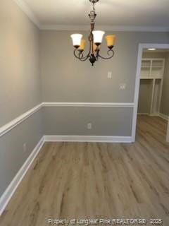 unfurnished dining area featuring ornamental molding, an inviting chandelier, and wood finished floors