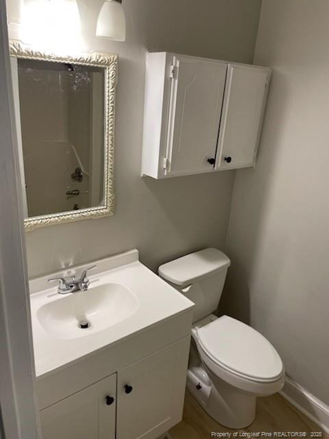 bathroom featuring toilet, baseboards, walk in shower, and vanity