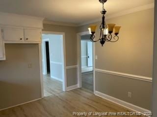 unfurnished dining area with a chandelier, crown molding, baseboards, and wood finished floors