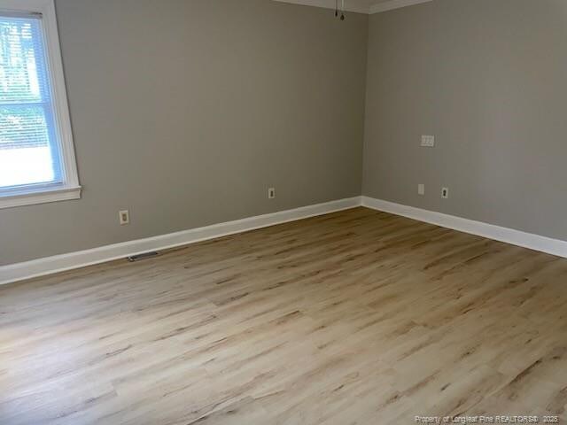 unfurnished room with crown molding, wood finished floors, visible vents, and baseboards