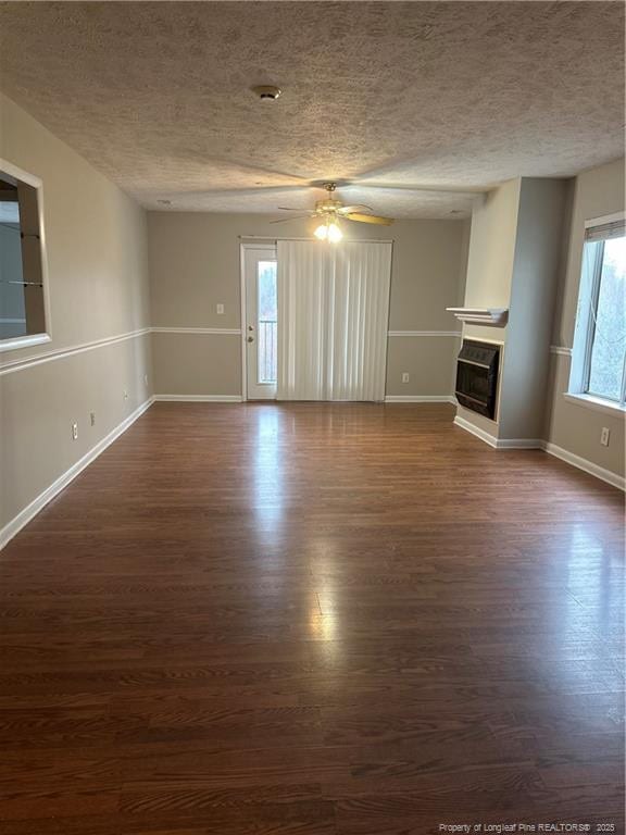 unfurnished living room with dark wood-style floors, a textured ceiling, a fireplace, and baseboards