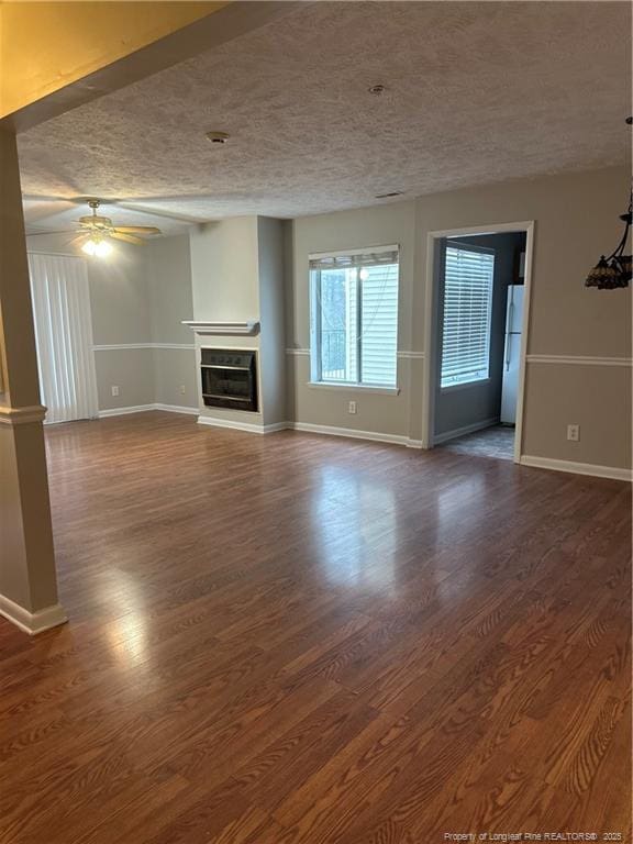 unfurnished living room featuring ceiling fan, a textured ceiling, baseboards, dark wood-style floors, and a glass covered fireplace