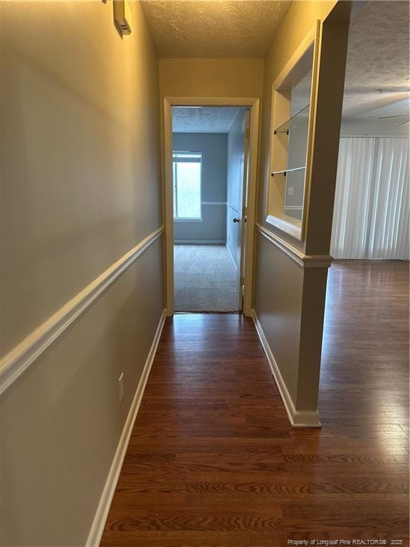 hallway featuring dark wood-style flooring, a textured ceiling, and baseboards