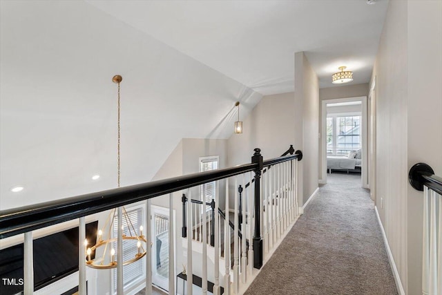 hall featuring baseboards, lofted ceiling, carpet, an upstairs landing, and a notable chandelier