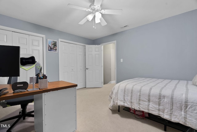 bedroom featuring multiple closets, light colored carpet, visible vents, and a ceiling fan