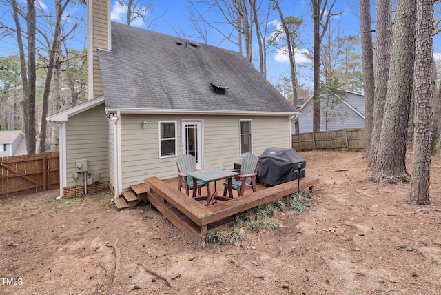 rear view of house with a chimney, fence, a deck, and roof with shingles