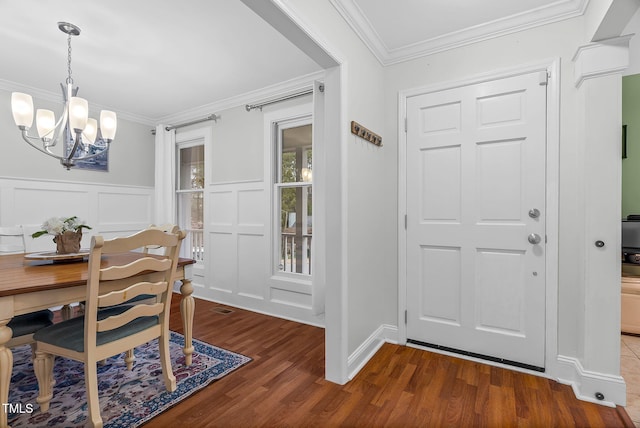 foyer featuring a notable chandelier, a decorative wall, dark wood finished floors, and crown molding