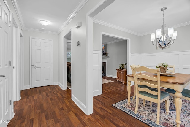 dining area featuring a decorative wall, crown molding, a fireplace, dark wood finished floors, and an inviting chandelier