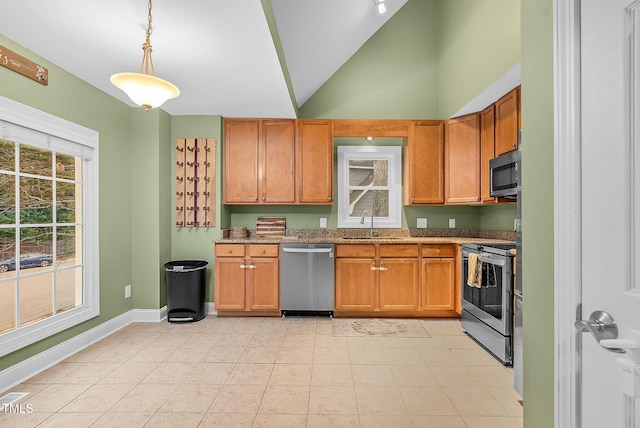 kitchen featuring stainless steel appliances, a sink, baseboards, dark stone countertops, and decorative light fixtures