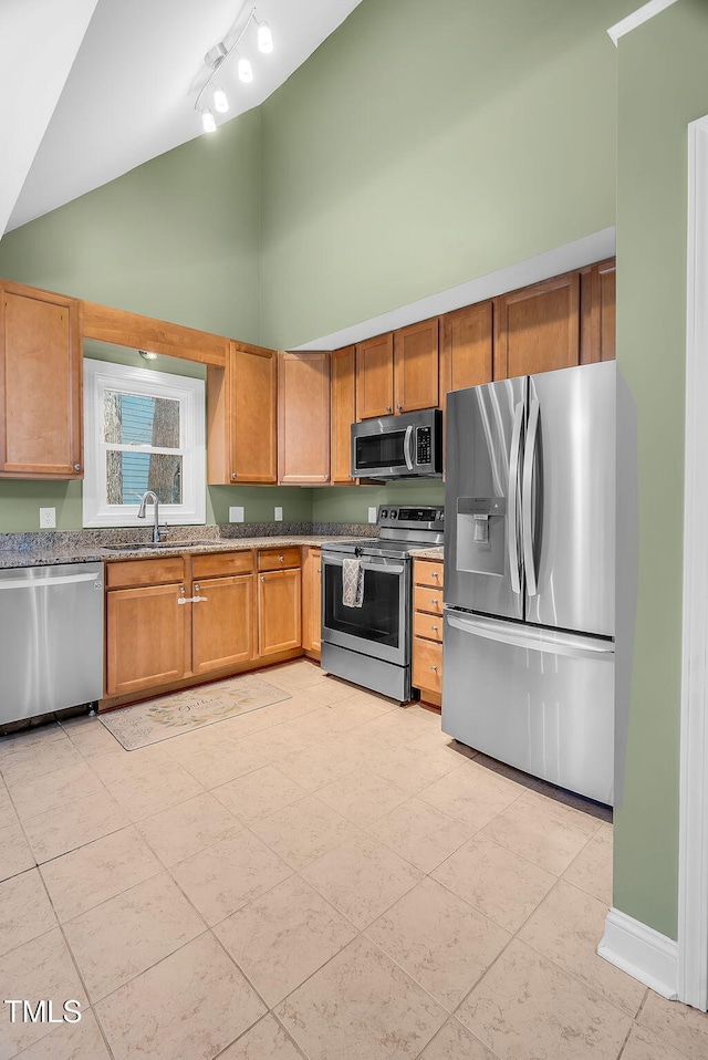 kitchen with high vaulted ceiling, stone countertops, stainless steel appliances, a sink, and baseboards