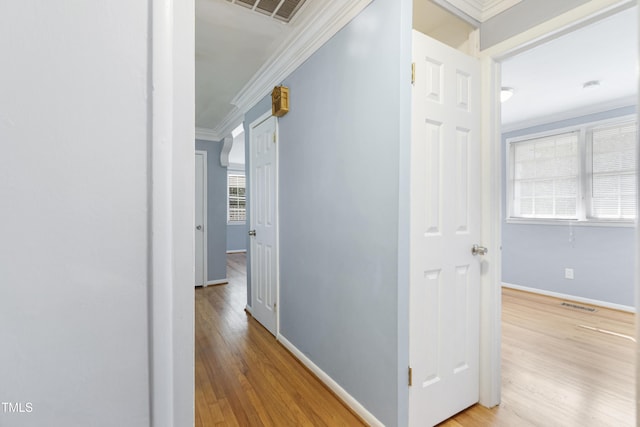 hallway featuring light wood-type flooring, visible vents, crown molding, and baseboards