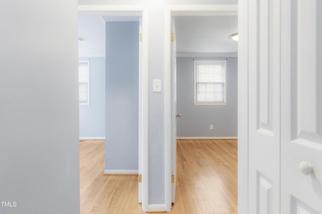 hallway featuring ornamental molding, light wood-type flooring, and baseboards