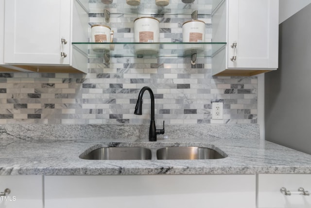 kitchen featuring open shelves, a sink, white cabinetry, and light stone countertops