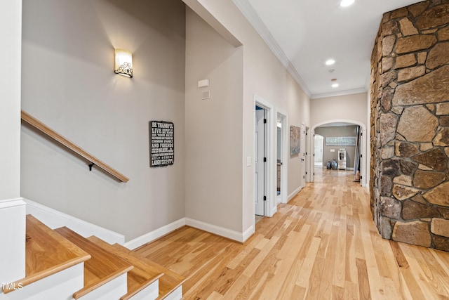 corridor with light wood finished floors, baseboards, arched walkways, ornamental molding, and recessed lighting