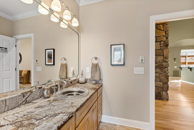 bathroom with wood finished floors, vanity, baseboards, visible vents, and crown molding