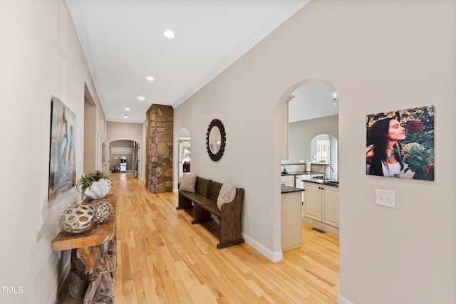 hall with light wood finished floors, baseboards, arched walkways, ornamental molding, and a sink