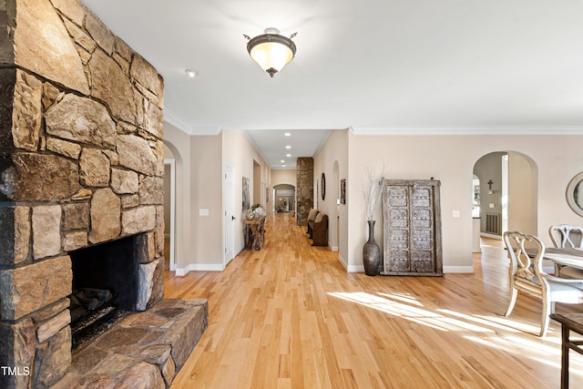 foyer with ornamental molding, arched walkways, a fireplace, and light wood finished floors