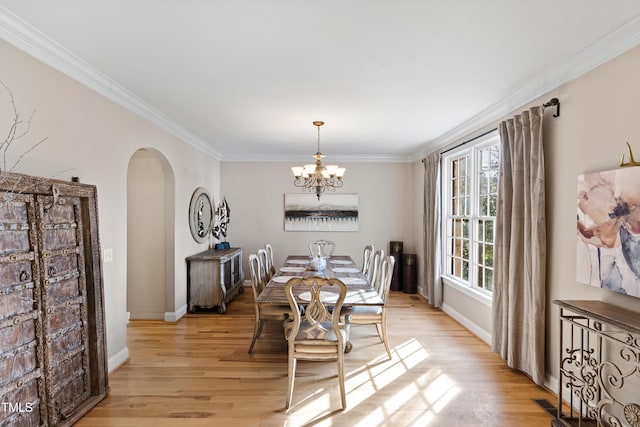 dining space with ornamental molding, arched walkways, a chandelier, and light wood finished floors