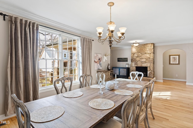 dining room featuring arched walkways, baseboards, light wood-style flooring, ornamental molding, and an inviting chandelier