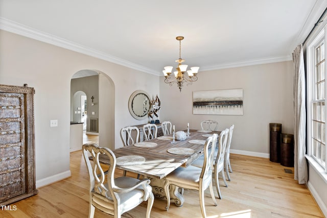 dining space with light wood-type flooring, baseboards, arched walkways, and crown molding