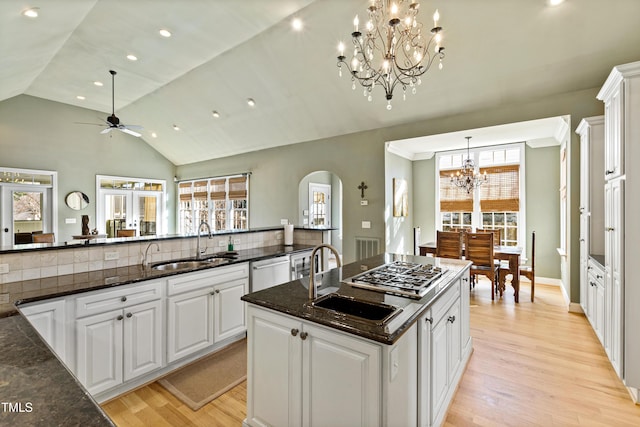 kitchen featuring arched walkways, stainless steel appliances, light wood-style floors, white cabinetry, and a sink