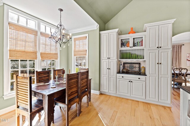 dining area featuring baseboards, arched walkways, lofted ceiling, light wood-style floors, and a chandelier