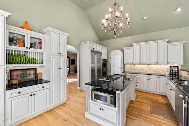 kitchen with stainless steel appliances, arched walkways, white cabinets, and light wood-style floors