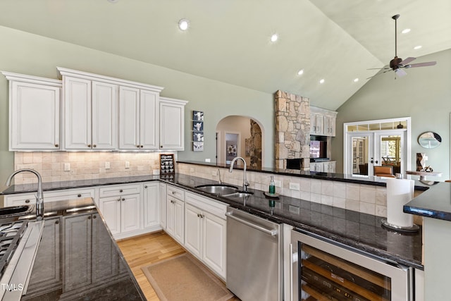 kitchen featuring beverage cooler, arched walkways, a sink, light wood-style floors, and stainless steel dishwasher