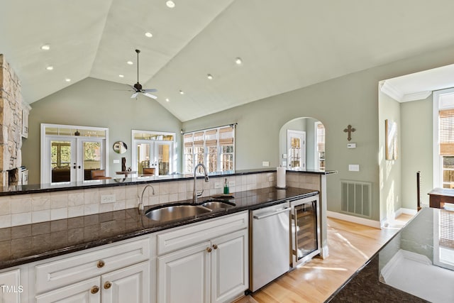 kitchen featuring beverage cooler, visible vents, dark stone countertops, stainless steel dishwasher, and a sink